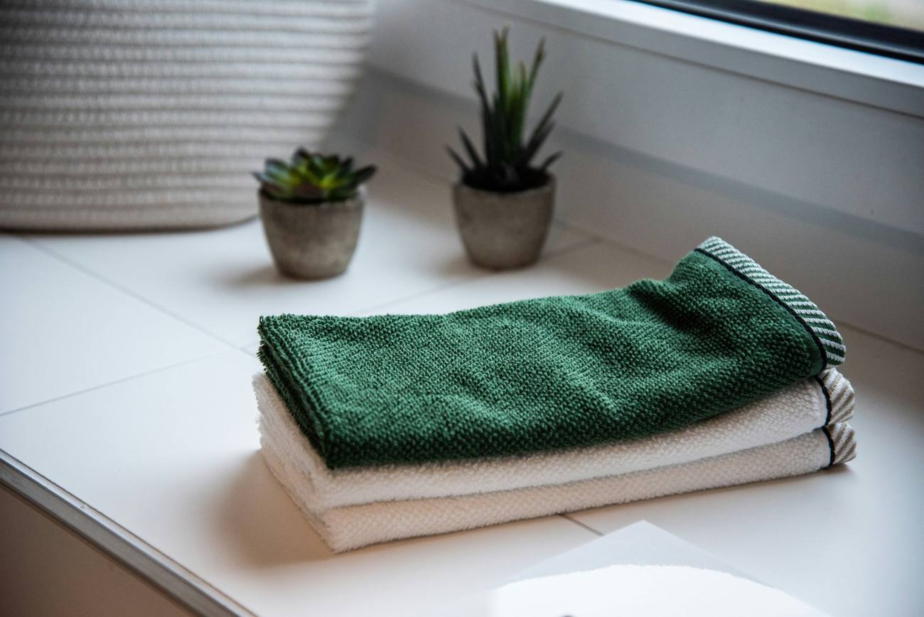 Folded green and white towels beside small plants